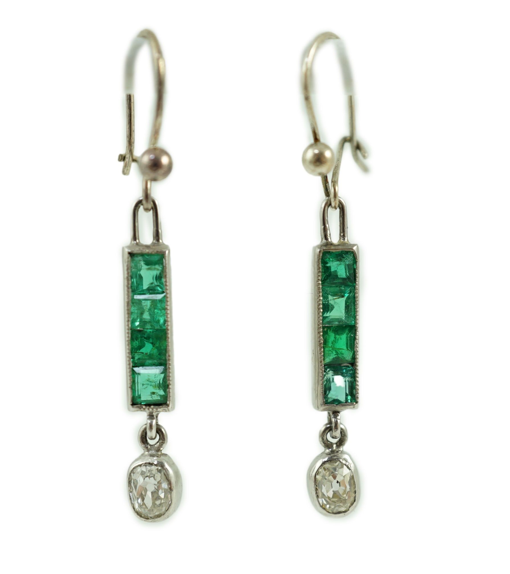 A pair of white gold, four stone emerald and single stone oval cut diamond set drop earrings